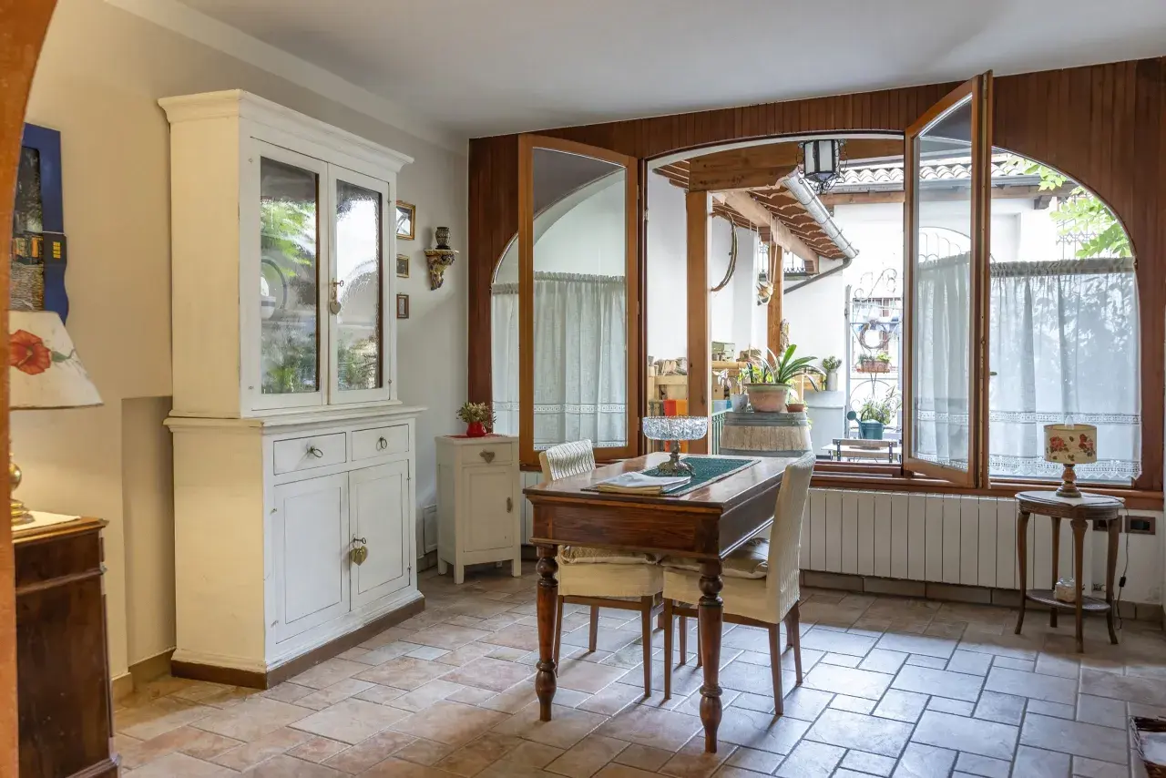 Un tavolo da pranzo con sedie, un mobile bianco e un'ampia finestra che si apre su un cortile. Il **motel significato** qui è un luogo accogliente, non solo un posto dove dormire.