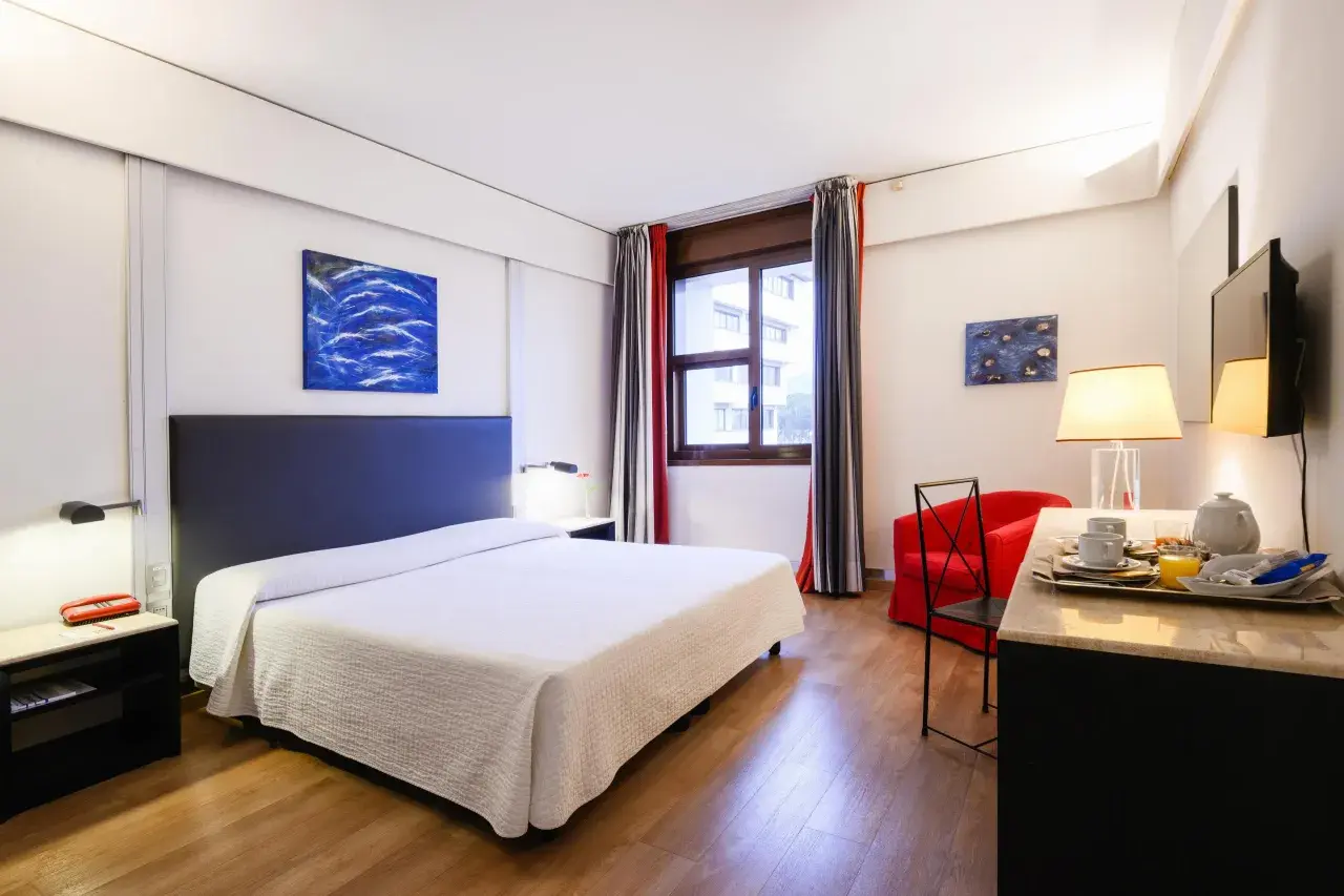 Camera accogliente con letto, poltrona rossa e vassoio colazione, perfetta per un day use rilassante.