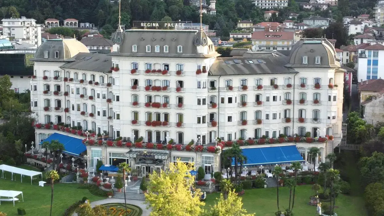 Hotel Regina Palace, un'elegante struttura con balconi fioriti. Forse stanno facendo un **ab testing** per vedere quale colore di tende blu attira più clienti.