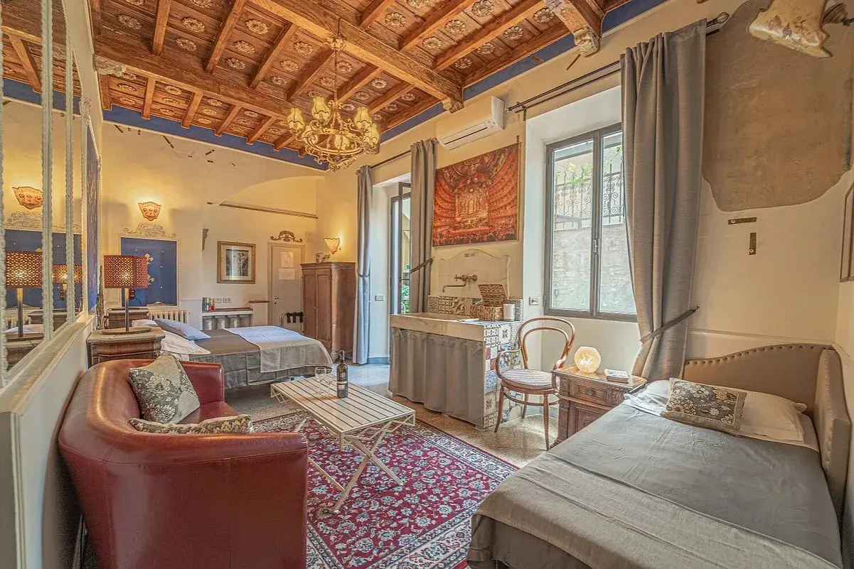 Camera accogliente in un hotel o b&b con soffitto in legno, divano rosso, due letti e un lavabo decorato.