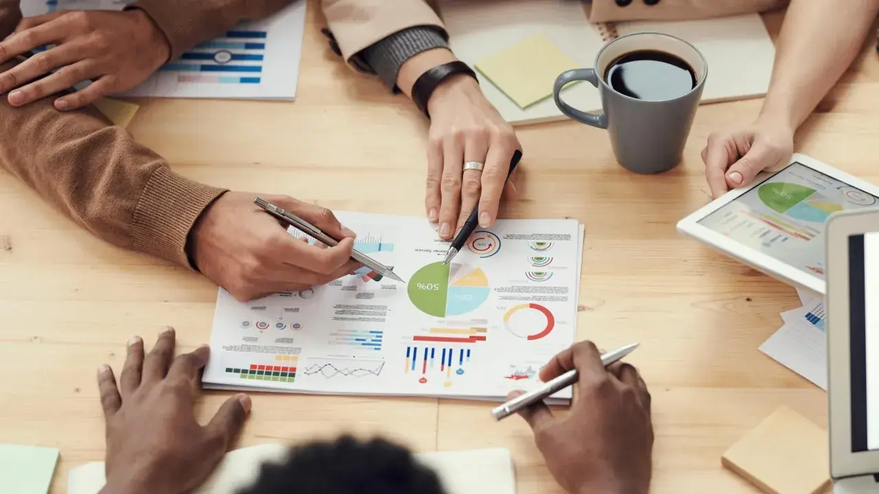 Persone analizzano grafici e dati su un tavolo, discutendo le impostazioni OTA (Over-The-Air) per aggiornamenti software.