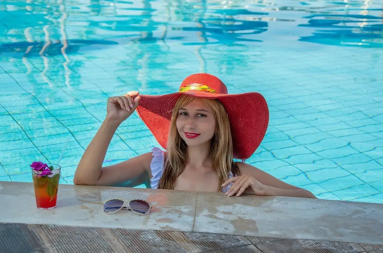 Donna con cappello rosso in piscina, sorseggia un cocktail. Cosa significa guest? Essere coccolati e rilassati, proprio come lei.