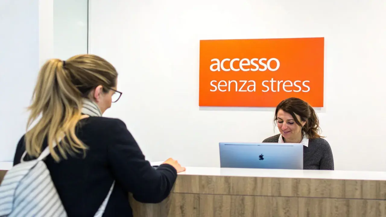 Una donna alla reception, con un cartello "accesso senza stress" sopra, sembra avere problemi con il suo computer.