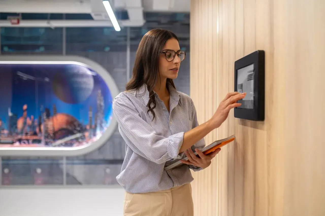 Donna interagisce con un pannello touch, parte dell'automazione hotel, tenendo un tablet.