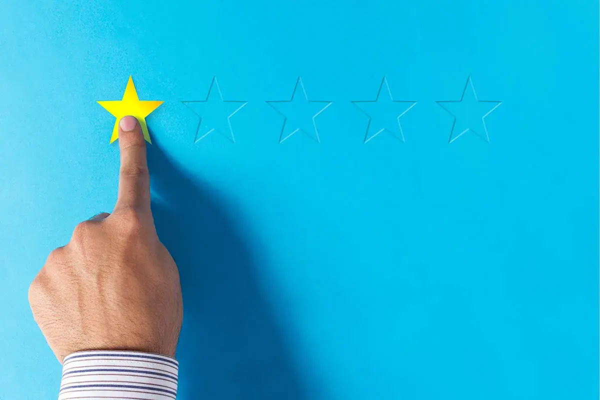 Dito, una mano seleziona una stella gialla, lasciando le altre vuote. Un'immagine che evoca le recensioni negative sui booking.