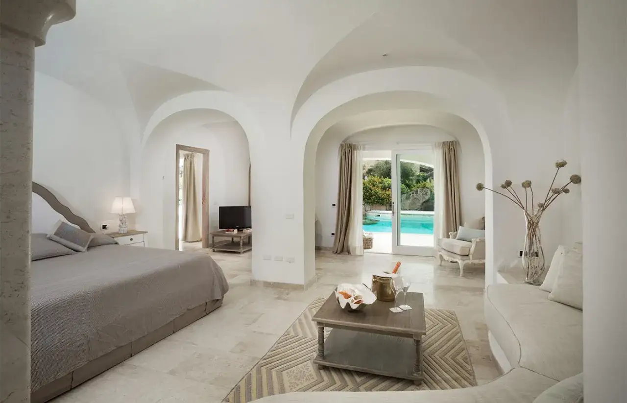 Camera da letto con piscina, perfetta per un booking fotografico. Archi bianchi, letto comodo, TV, e un tavolino con champagne.