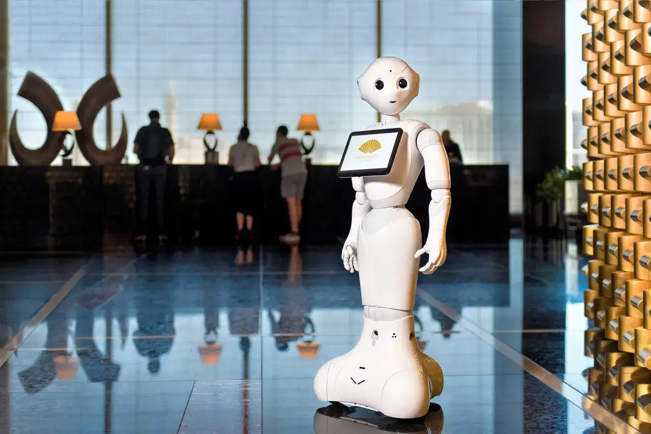 Un hotel robot bianco accoglie gli ospiti in un lussuoso atrio. Sullo schermo del robot, il logo Mandarin Oriental.