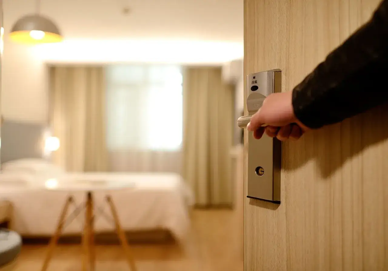 Mano che apre la porta di una camera d'albergo, un invito a scoprire i servizi dell'attività alberghiera.