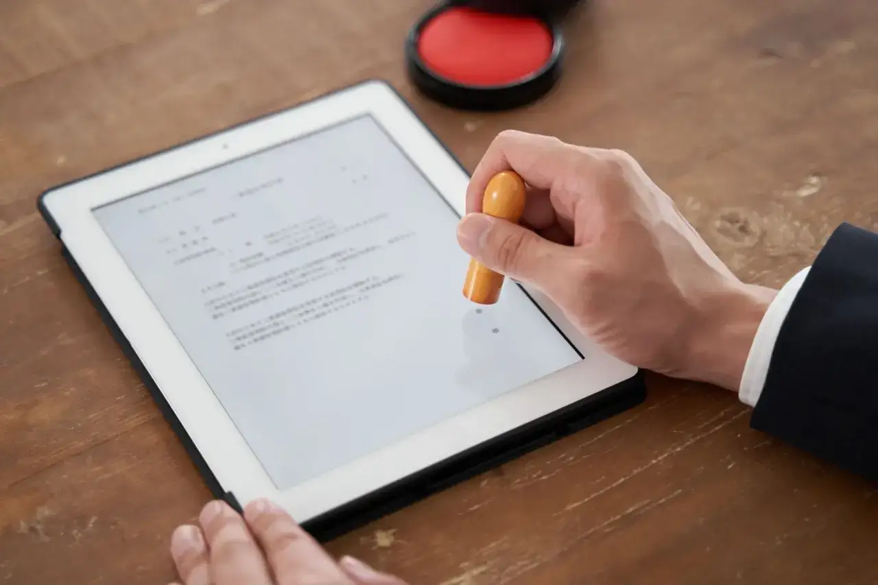 Mano che usa un sigillo per apporre una firma digitale su un documento visualizzato su un tablet.