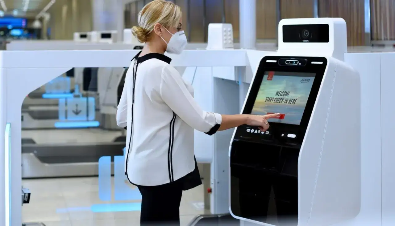 Donna con mascherina usa un totem per il check in express in aeroporto.