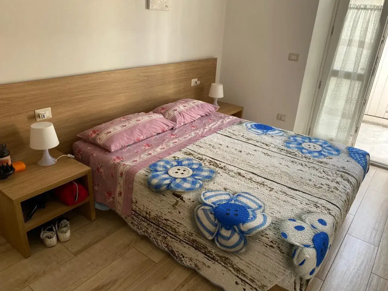 Camera da letto accogliente, perfetta per chi vuole capire come aprire una casa vacanze. Lenzuola floreali e copriletto con fiori blu.
