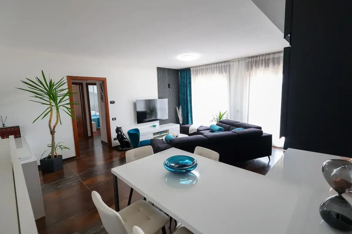 Soggiorno moderno e luminoso, ideale per una locazione turistica. Divano angolare, TV, tavolo da pranzo e porta aperta su un'altra stanza.