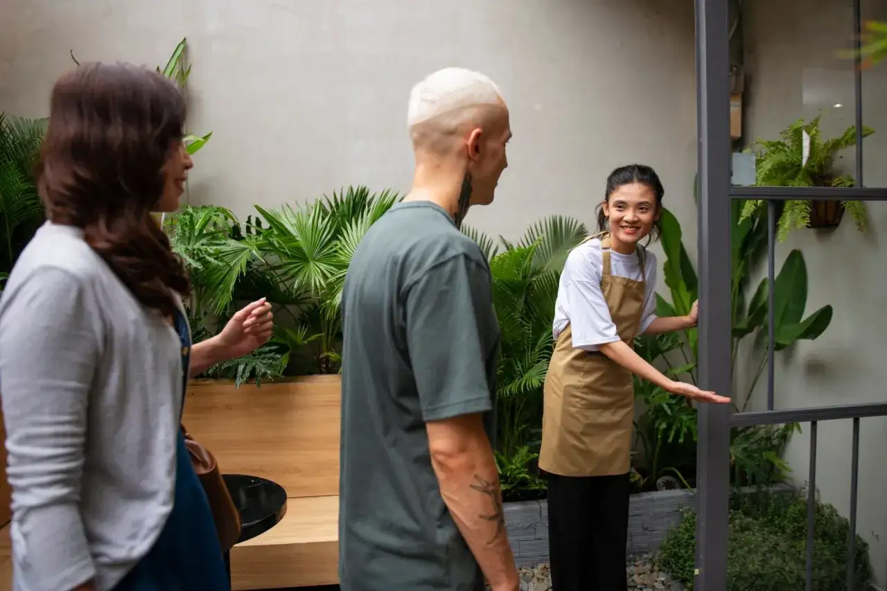 Un addetto al front office accoglie due clienti in un locale con molte piante.